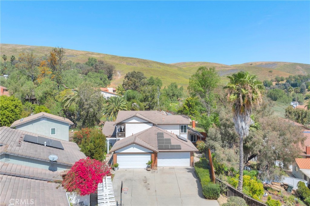 Aerial view of 3675 Cypress Ln, a two-story Yorba Linda home set against rolling open hills and trails, with a long private driveway and mature palms